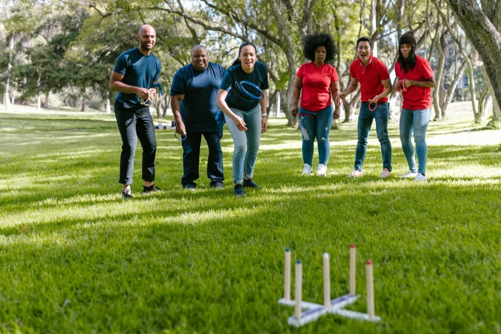 Group of diverse adults playing a ring toss game in a sunny park, promoting teamwork and fun.